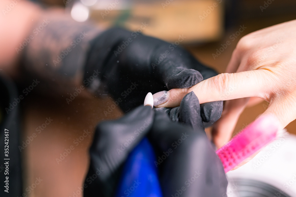 Naklejka premium Female master uses an electric machine to remove the nail polish during manicure in the salon. Close-up hardware manicure. Concept of hand care. Female manicurist cleaning of nails by a milling cutter