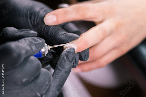 Woman use electric nail file drill in beauty salon. Nails manicure process in detail. Gel polish close-up concept.