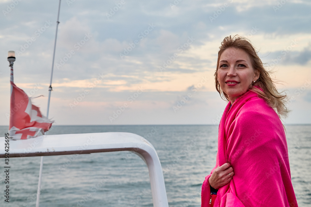 Fototapeta premium Girl in red scarf resting on a boat on water of sea or ocean in the evening.