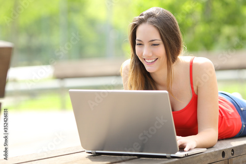 Happy woman with laptop lying on a park bench