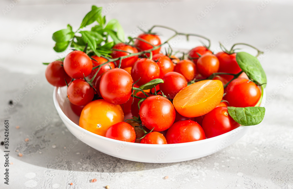 Red cherry and yellow tomatoes with baby spinach on the white plate. Healthy food, vegan or diet nutrition concept. Red cherry and yellow tomatoes with baby spinach on the white plate. Healthy food, vegan or diet nutrition concept.