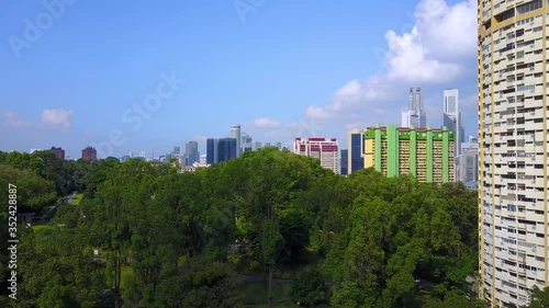 Smooth steady low directional aerial drone flight over lush green trees or forest revealing futuristic Singapore city skyline apartment skyscrapers and high rises on a sunny humid day photo