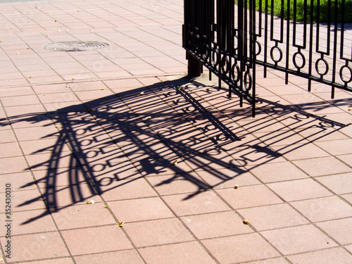 Metal gate and fence and its shadow on the pavement
