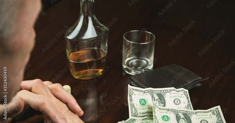 retired man sits at brown wooden table near banknotes by wallet and alcohol in bottle retired man sits at brown wooden table near banknotes by wallet and alcohol in bottle