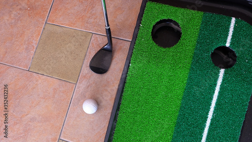 Golf putting mat, with a golf club and a ball at the side. Top view.