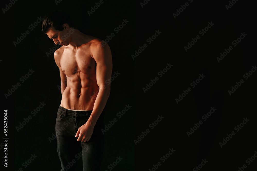 Horizontal view of a strong athletic handsome man with naked torso on dark black background. Copy space. Horizontal view of a strong athletic handsome man with naked torso on dark black background. Copy space.