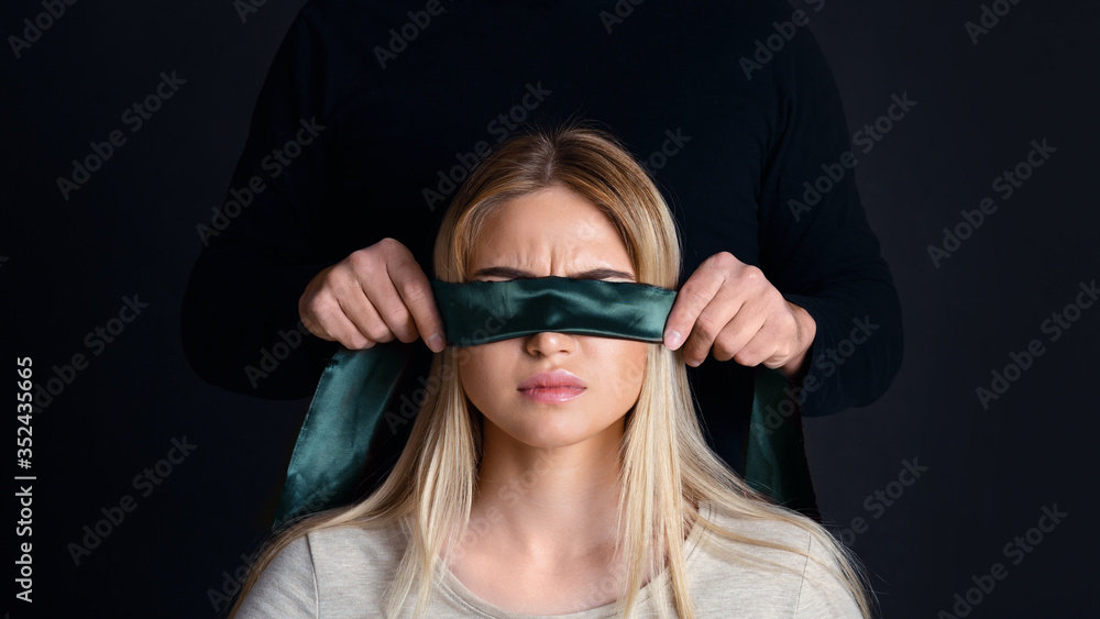 Abuzer concept. Man in black tying female eyes with green ribbon Abuzer concept. Man in black tying female eyes with green ribbon