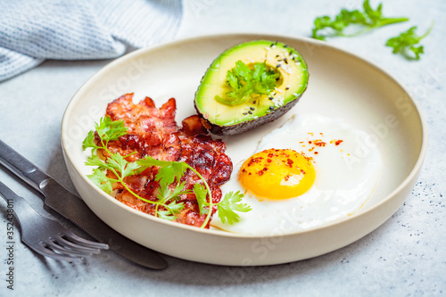 Keto breakfast - fried egg, avocado and fried bacon in white plate. Keto diet concept.