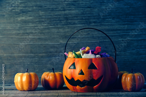 The candy that the children received as a gift put in a pumpkin-shaped basket which had a cool face decorate with small pumpkin on old wood table, halloween party concept