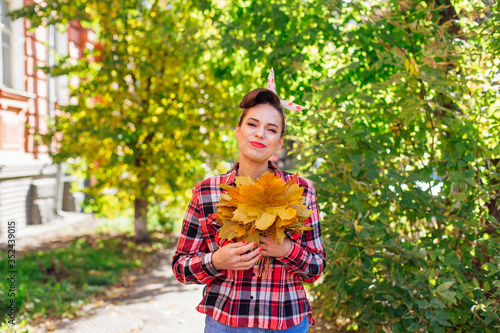 Beautiful woman with make up and hair in pin up style holding big bouquet of maple yellow leaves. photo