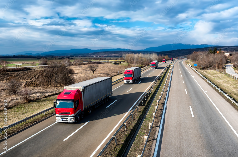 Fleet of Red Trucks in line as a convoy at a rural countryside highway under a beautiful blue sky