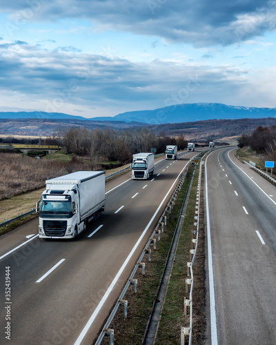 Fleet of White Trucks in line as a convoy at a rural countryside highway under a beautiful blue sky