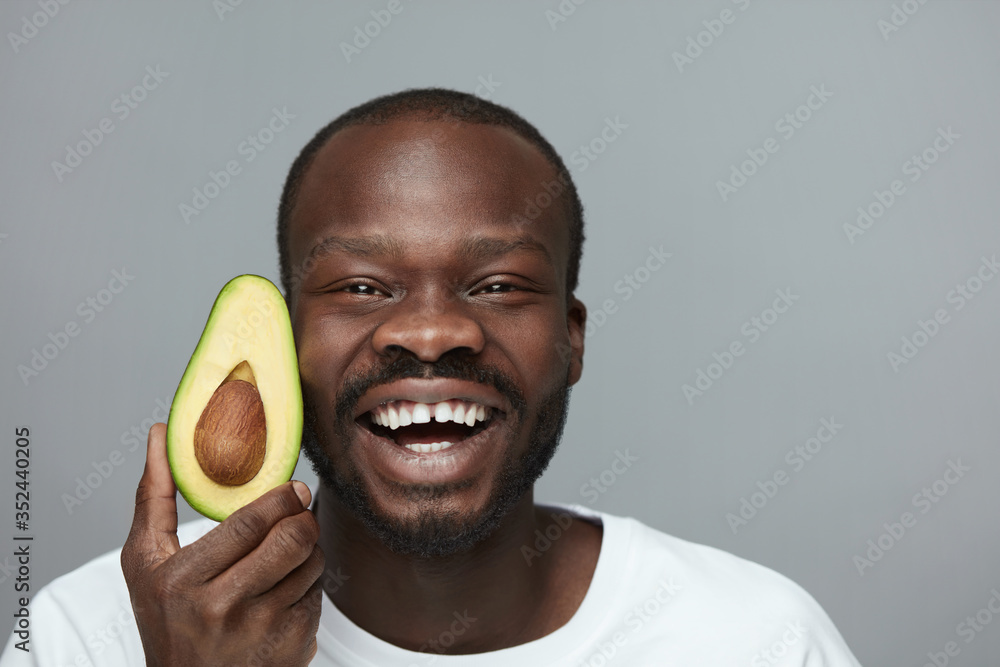 Avocado For Health. Facial Skincare Treatment With Natural Vitamins. Male African Model Holds Fresh Fruit Near Face. - obrazy, fototapety, plakaty 