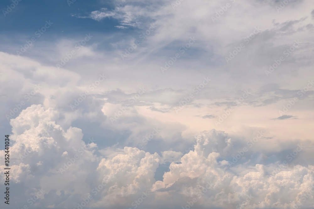 Fluffy white cumulus clouds developing into thunderheads, with some blue sky and sunlight, creating a beautiful cloudscape.