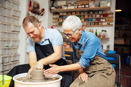 Senior woman spinning clay on a wheel with teacher at pottery class