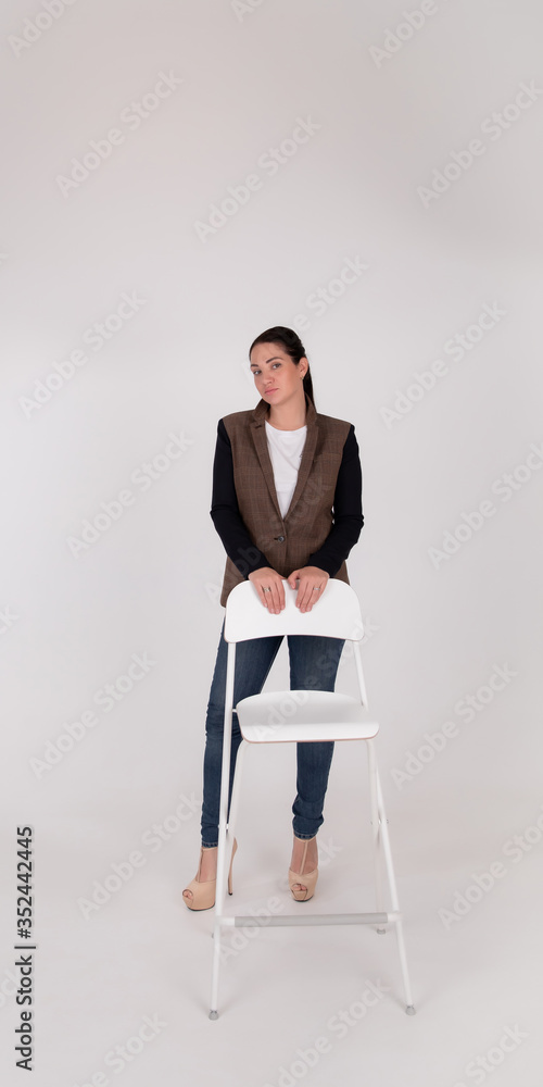 Successful business woman on grey background with copy space. In full height stands next to the white chair Successful business woman on grey background with copy space. In full height stands next to the white chair