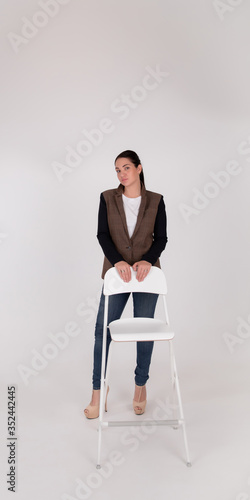 Successful business woman on grey background with copy space. In full height stands next to the white chair
