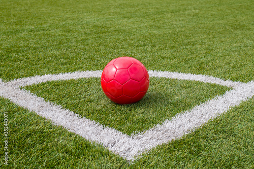 a red soccer ball lies in the corner of the soccer field next to the line