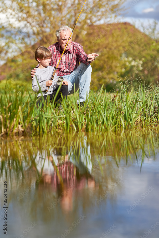 Fototapeta premium Opa zeigt seinem Enkelsohn das Angeln am See