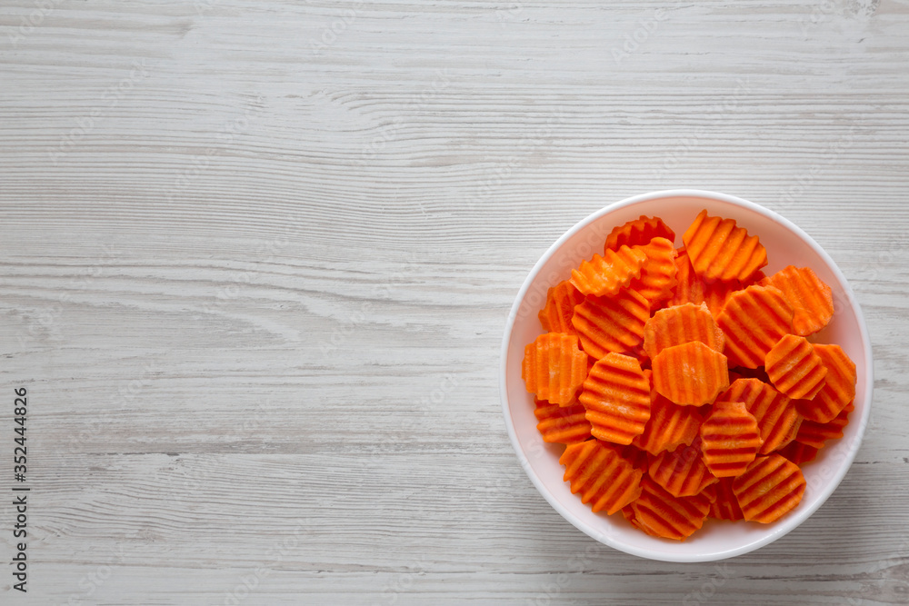 Fresh Raw Organic Carrot Chips in a white bowl on a white wooden background, top view. From above, overhead, flat lay. Space for text. Fresh Raw Organic Carrot Chips in a white bowl on a white wooden background, top view. From above, overhead, flat lay. Space for text.