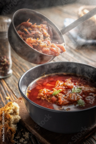 Tomato soup with vegetables and meat is poured into a bowl from the ladle from which steam comes, tasty, appetizing traditional Ukrainian borsch, close-up, shallow depth of field, selective focus