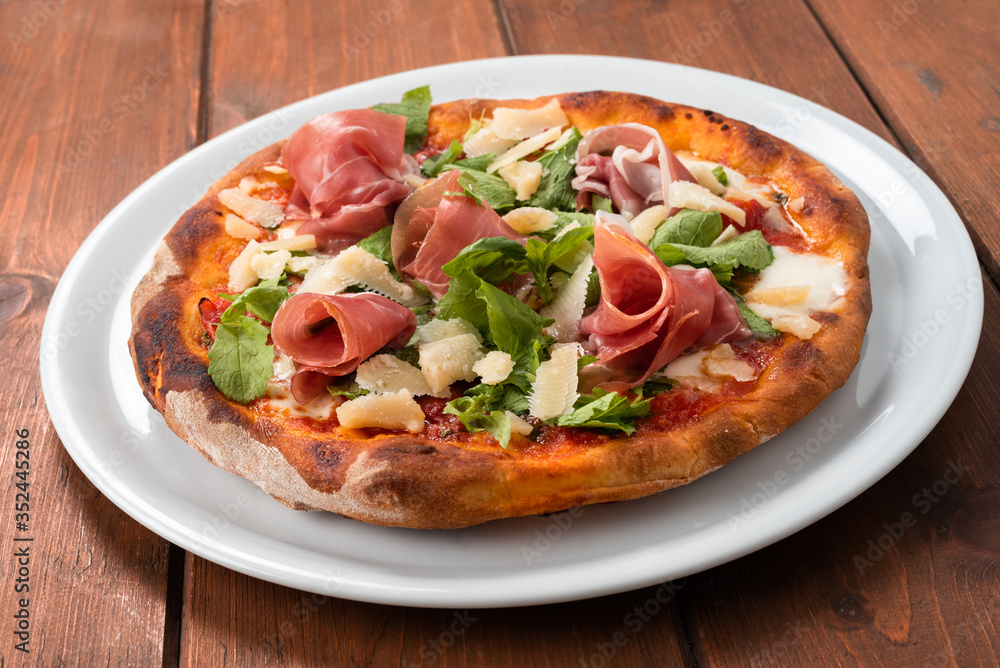 Deliziosa pizza emiliana con fette di prosciutto crudo, parmigiano e insalata 