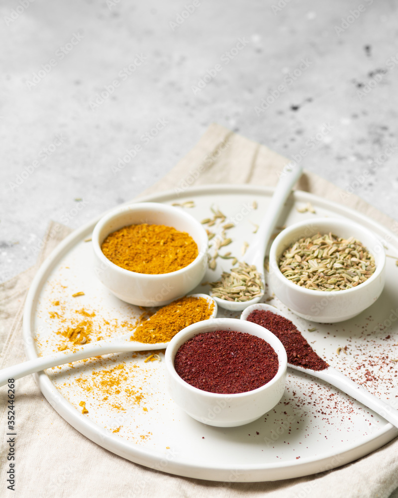 Spices and condiments in white bowls on a light gray table. Turmeric, ginger, curry, fennel and sumac in white bowls. Spices close up Spices and condiments in white bowls on a light gray table. Turmeric, ginger, curry, fennel and sumac in white bowls. Spices close up