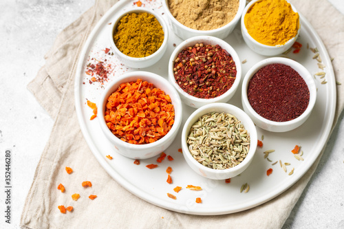 Fototapeta Naklejka Na Ścianę i Meble -  Spices and condiments in white bowls on a light gray table. Turmeric, ginger, curry, fennel and sumac in white bowls. Spices close up