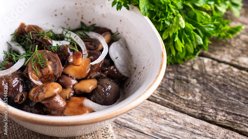 Pickled mushrooms with onion in a bowl on wooden background. Copy space
