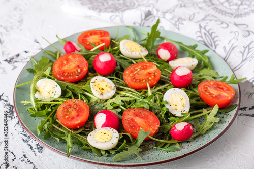 Healthy salad with tomatoes, quail eggs, arugula and radish on a plate. Diet food concept.