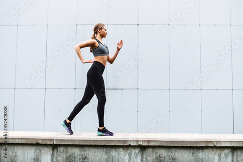 Cheerfulness for full day long. An attractive young woman is jogging outdoors. Side view. Healthy lifestyle concept