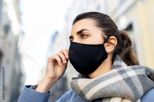 health, safety and pandemic concept - young woman wearing black face protective reusable barrier mask in city