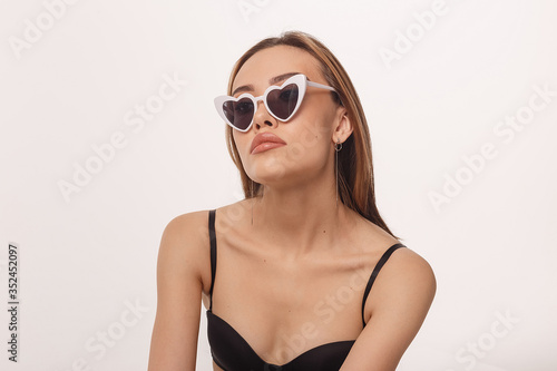 portrait of sexy asian woman with long hair, heart shaped sunglasses posing in black lingerie isolated on white background. model tests of skinny girl in bra. attractive female poses in studio
