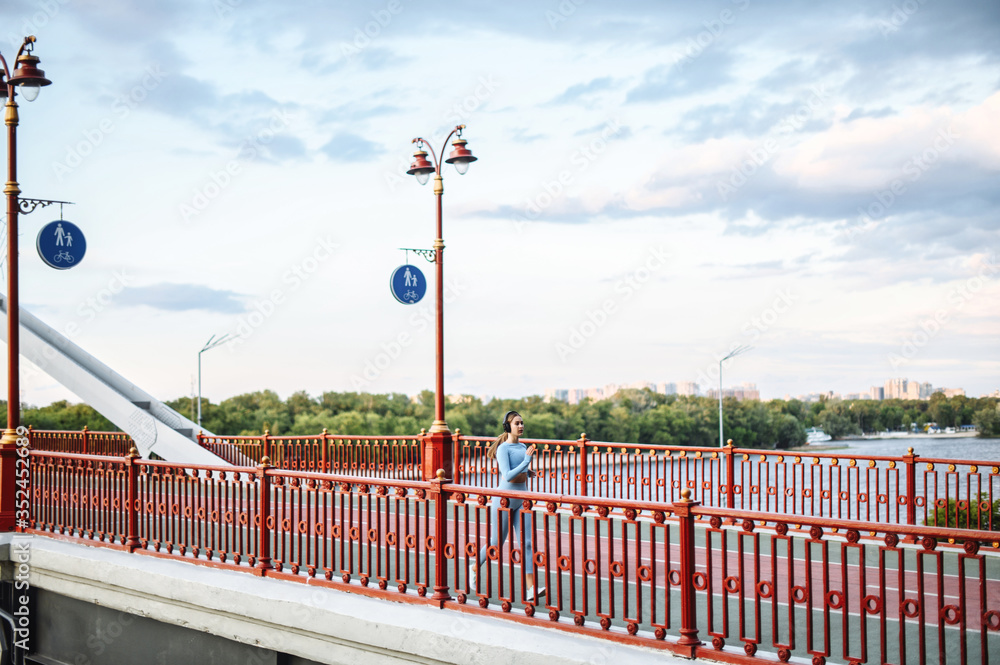 Jog in the city. Runner woman is jogging on a city bridge, the river side on background