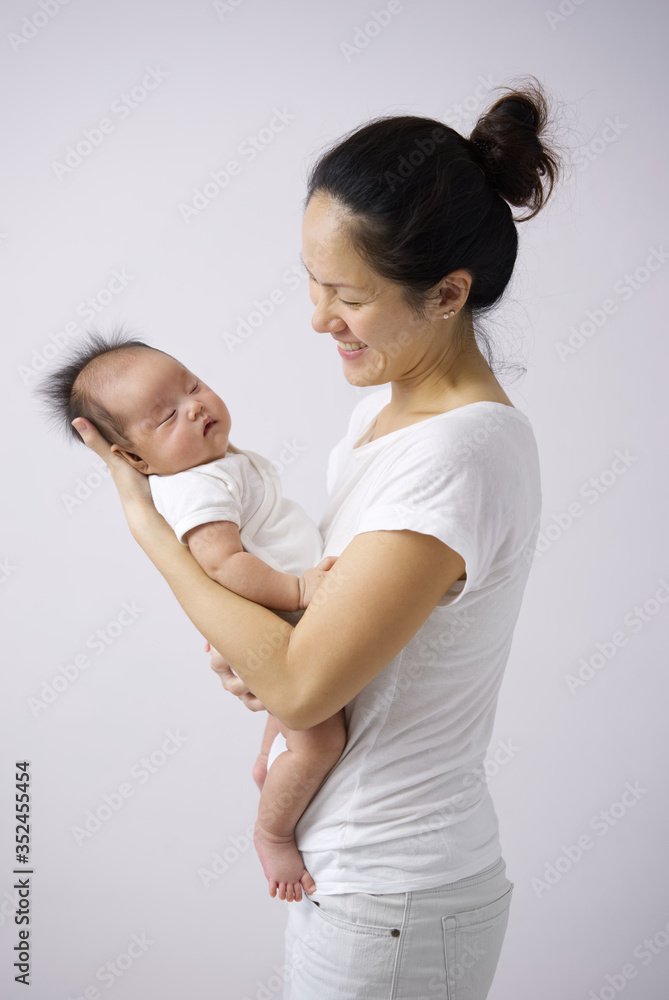 Asian chinese mother carrying her newborn child indoors with pink background Asian chinese mother carrying her newborn child indoors with pink background