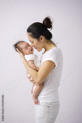 Asian chinese mother carrying her newborn child indoors with pink background