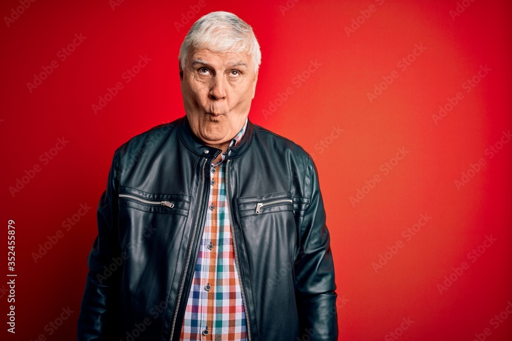 Senior handsome hoary man wearing casual shirt and jacket over isolated red background making fish face with lips, crazy and comical gesture. Funny expression.