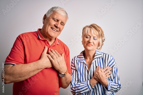 Senior beautiful couple standing together over isolated white background smiling with hands on chest with closed eyes and grateful gesture on face. Health concept.
