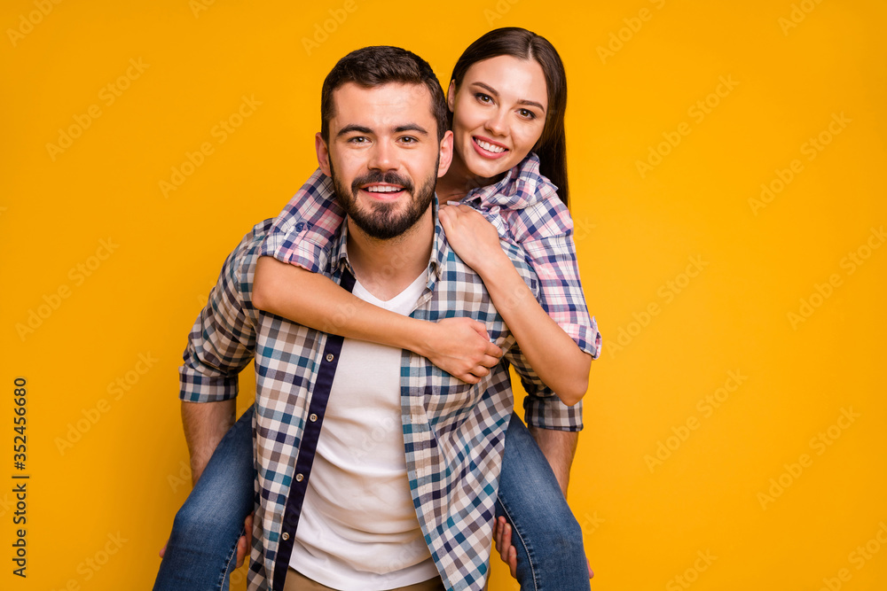 Portrait of positive cheerful married couple man carry piggyback woman enjoy summer rest relax wear checkered plaid shirt isolated over bright shine color background Portrait of positive cheerful married couple man carry piggyback woman enjoy summer rest relax wear checkered plaid shirt isolated over bright shine color background