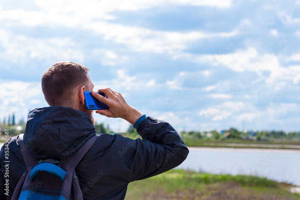 Bearded man in black raincoat on a blue sea landscape background with smartphone in hands talking. Middle aged guy calling friends on the cell phone on nature, people communication lifestyle concept. Bearded man in black raincoat on a blue sea landscape background with smartphone in hands talking. Middle aged guy calling friends on the cell phone on nature, people communication lifestyle concept.