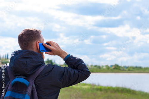 Bearded man in black raincoat on a blue sea landscape background with smartphone in hands talking. Middle aged guy calling friends on the cell phone on nature, people communication lifestyle concept.