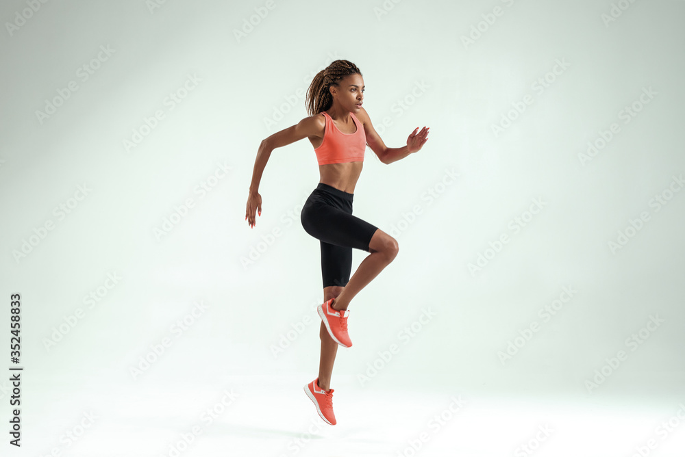 Higher and higher. Side view of young african woman with perfect body in sports clothing jumping while training in studio