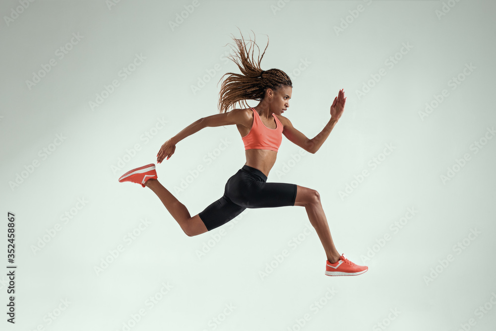 Never stop run. Full length of young african woman with perfect body in sports clothing jumping in studio against grey background