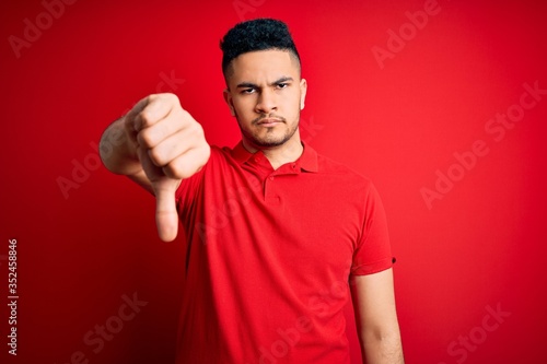 Young handsome man wearing red casual polo standing over isolated background looking unhappy and angry showing rejection and negative with thumbs down gesture. Bad expression. © Krakenimages.com