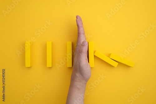 Fotografie a yellow domino block that begins to fall and a hand that prevents it from falling