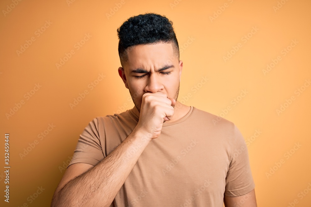 Young handsome man wearing casual t-shirt standing over isolated yellow background feeling unwell and coughing as symptom for cold or bronchitis. Health care concept. Young handsome man wearing casual t-shirt standing over isolated yellow background feeling unwell and coughing as symptom for cold or bronchitis. Health care concept.