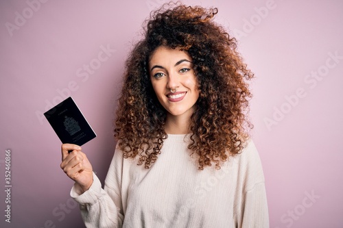 Beautiful tourist woman with curly hair and piercing holding canada canadian passport id with a happy face standing and smiling with a confident smile showing teeth
