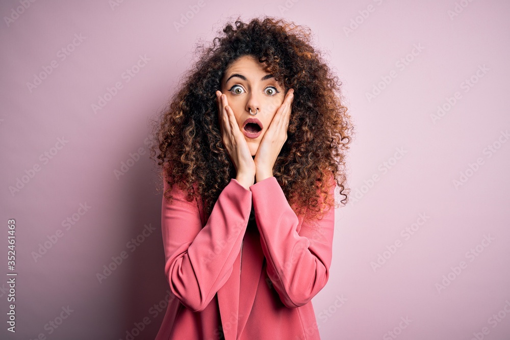 Young beautiful businesswoman with curly hair and piercing wearing elegant jacket afraid and shocked, surprise and amazed expression with hands on face Young beautiful businesswoman with curly hair and piercing wearing elegant jacket afraid and shocked, surprise and amazed expression with hands on face