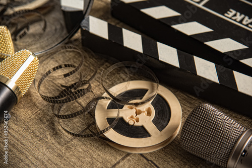 Film reel, movie clapperboard and two microphones on a table with
