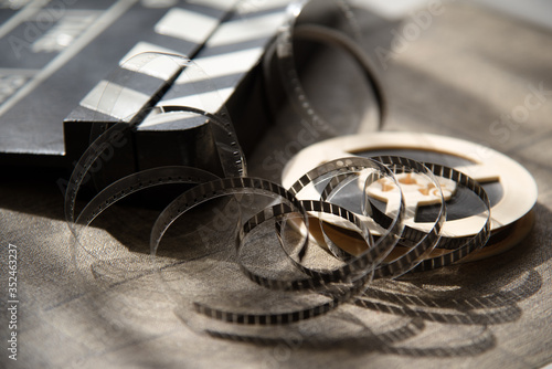 Unwound narrow retro film strip on a light reel with a movie clapperboard on a wooden table background.